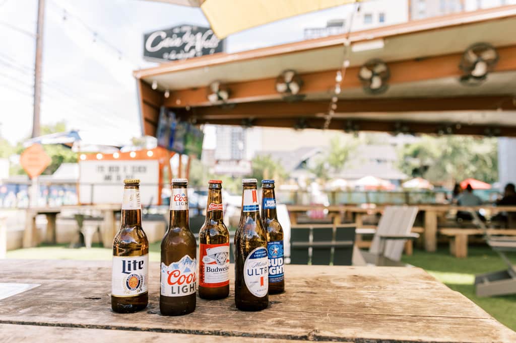Five ice-cold domestic bottles lined up on a Cabel's picnic table