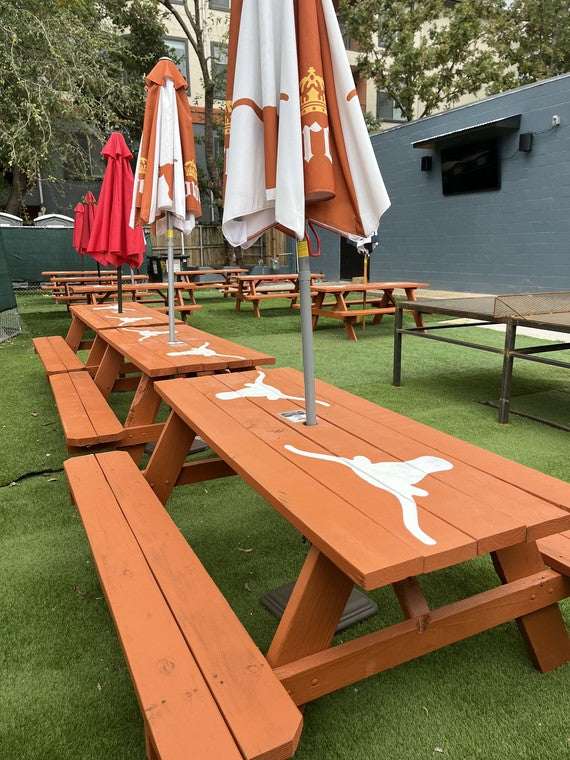 Burnt-orange picnic tables with the Longhorn logo, umbrellas at rest