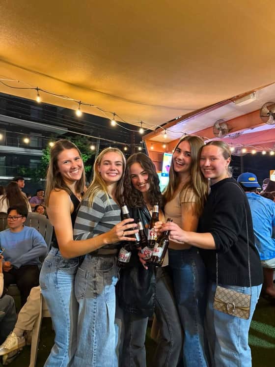 Five friends clinking beer bottles under the patio string lights at night