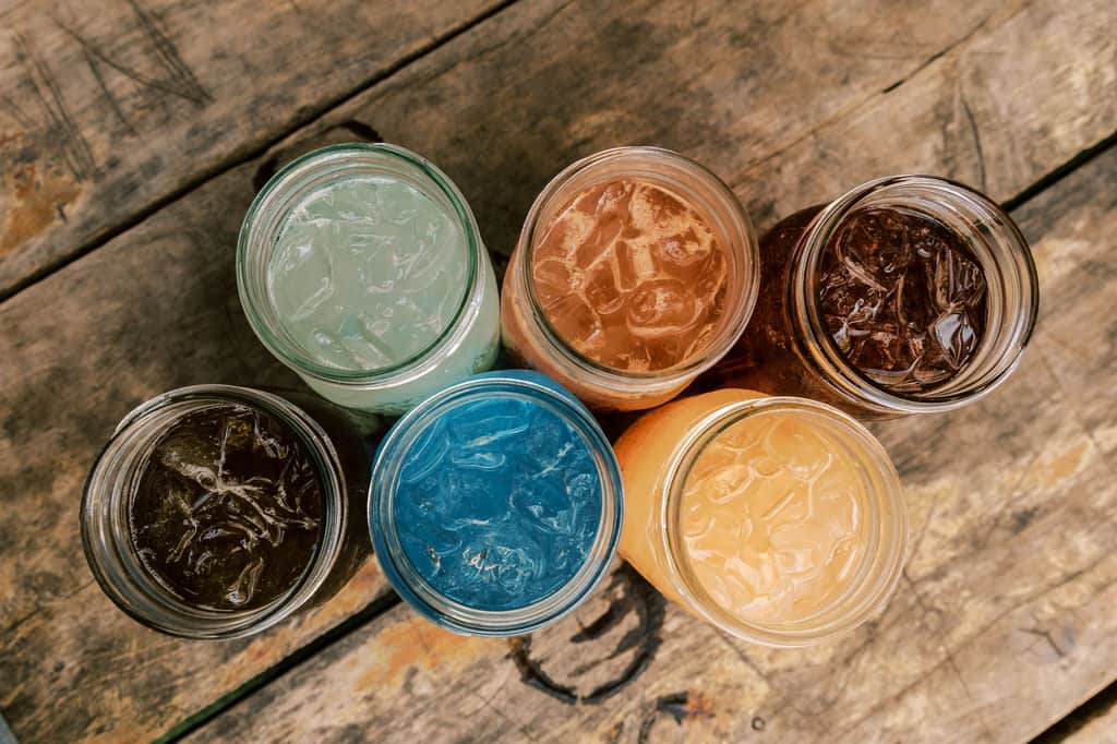 Six colorful mason-jar teas seen from above on weathered wood